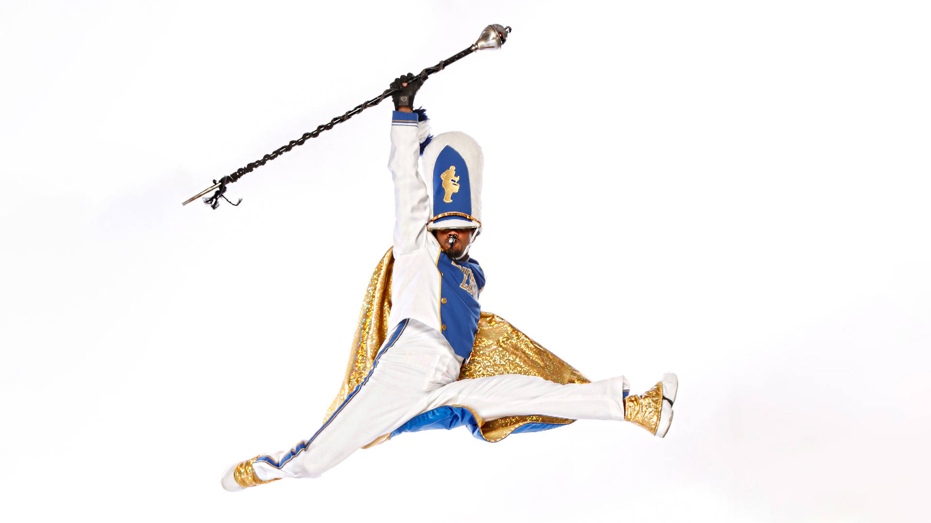 A Black drum major mid-leap with a whistle in mouth and baton raised with one hand against a white background. They are wearing a white uniform with blue accents and a gold shimmery cape.
