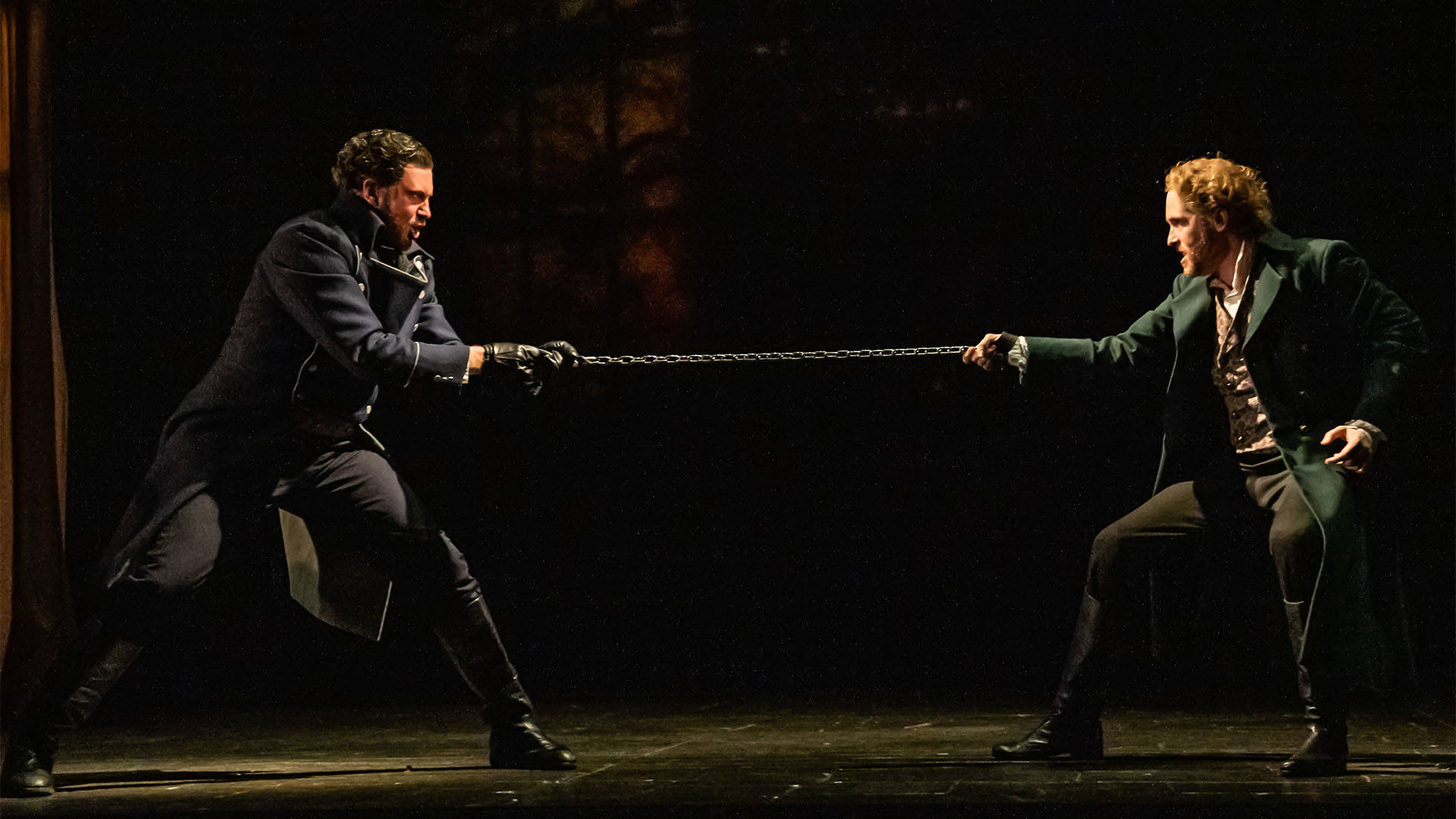 Two men in long coats struggle over a chain.