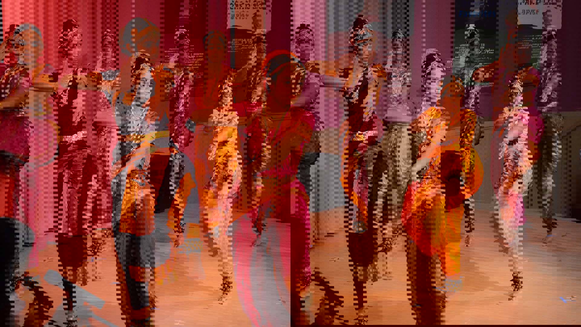 Six dancers performing on the Rotunda Stage wearing pink and yellow traditional Indian clothing and gold head ornaments.