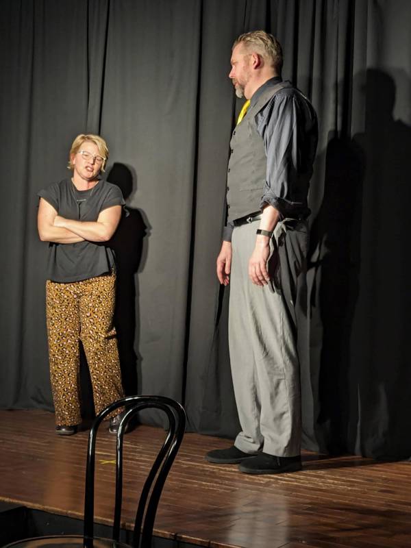 Jess Schuknecht performing improv. He is a white man with short hair and a beard. He is wearing a vest and tie and standing next to another performer with light complexion and blond hair.