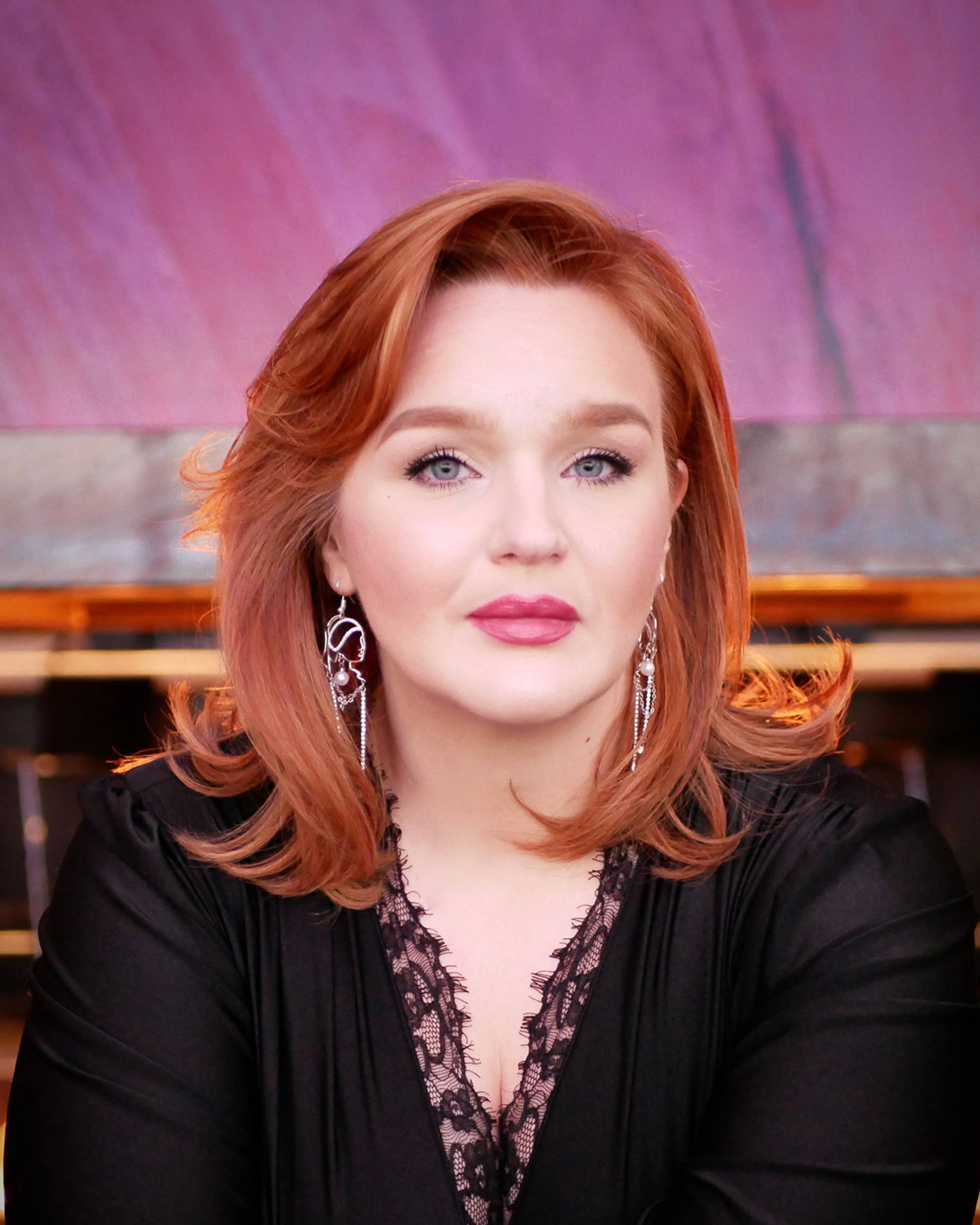 Headshot of a caucasian woman with red hair, blue eyes and a black top.