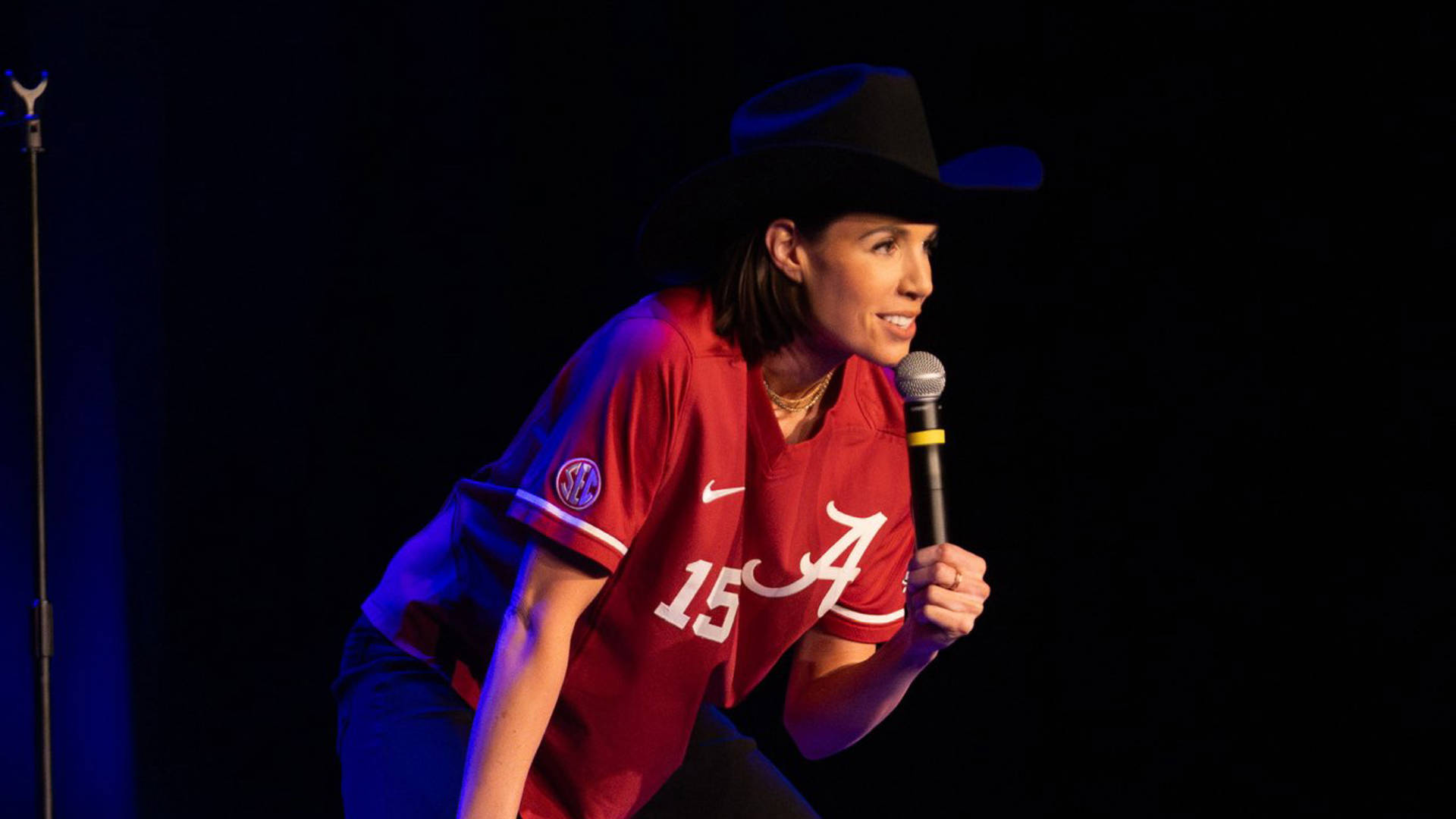 Danae Hays, a woman with light complexion, medium length brown hair, cowboy hat and an alabama sports short performing standup.