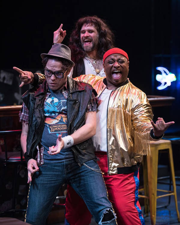 Three men in loud rock and roll outfits exclaiming towards the audience.