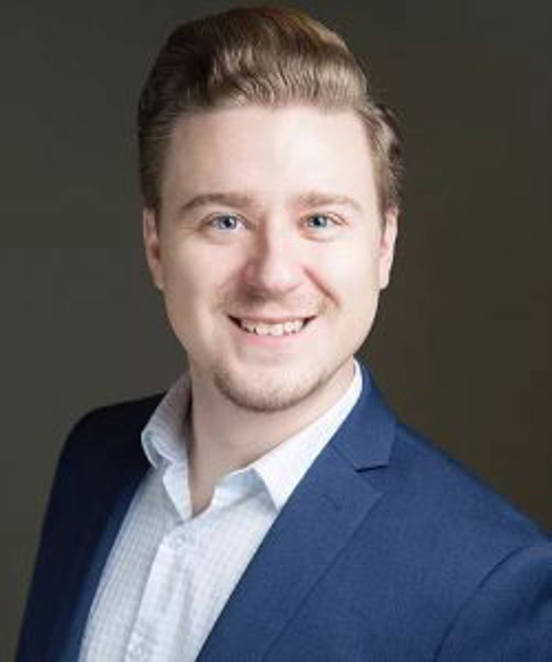 Headshot of a caucasian man with short blond hair and blue eyes in a blue suit.