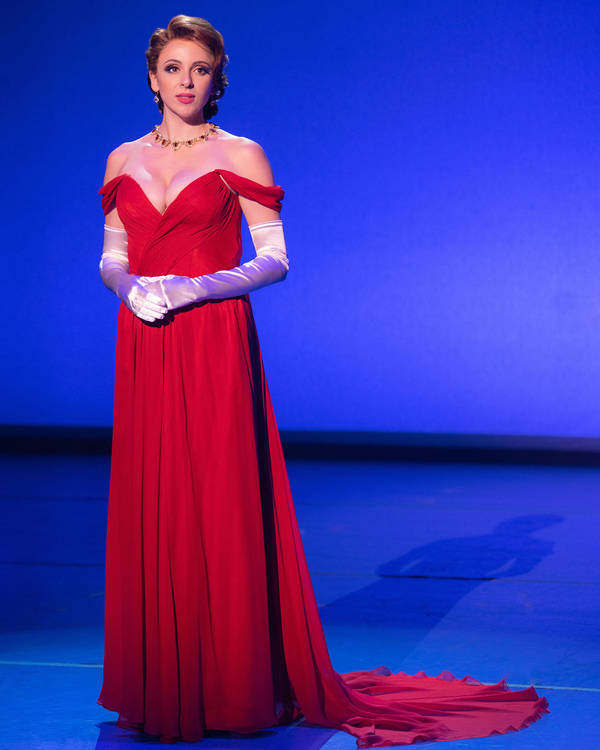 A caucasian woman in a red dress stands elegantly