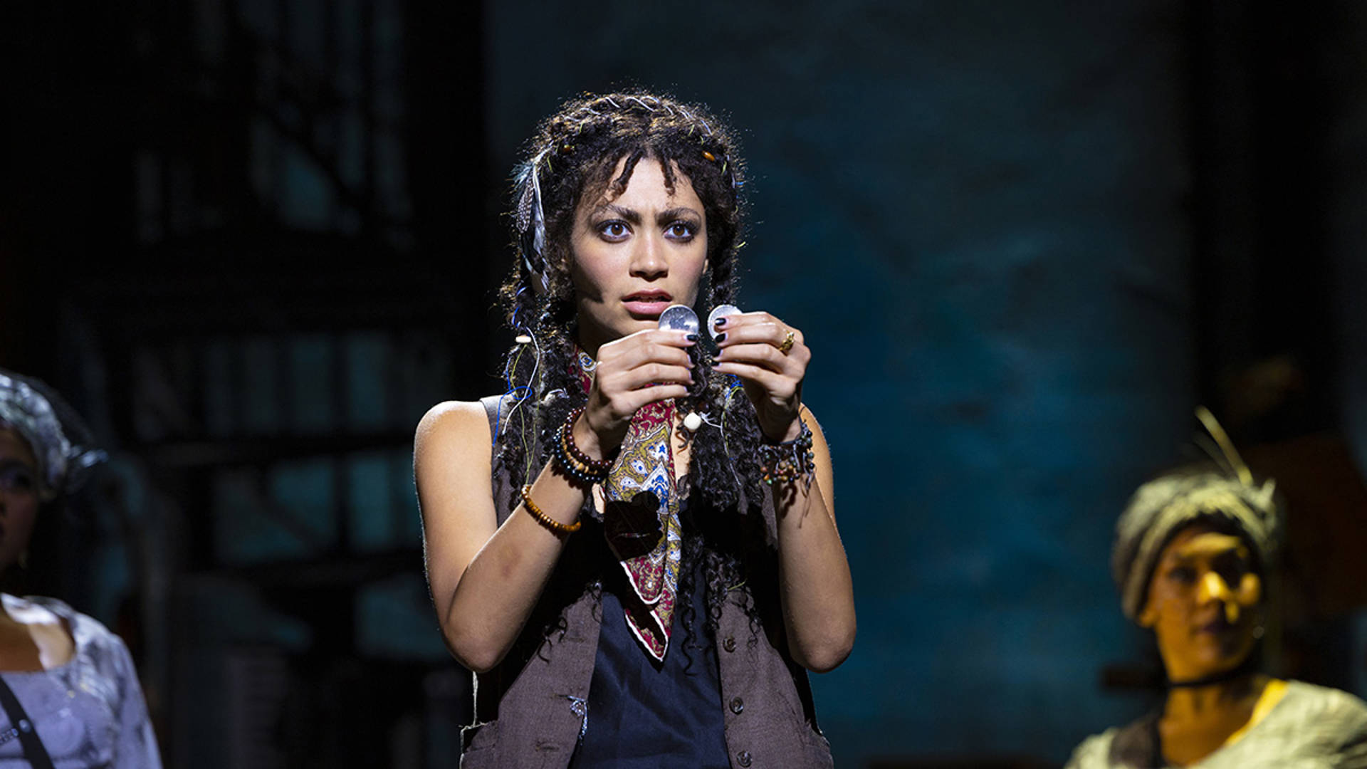 A young woman with dark brown hair holds two coins in front of her face.
