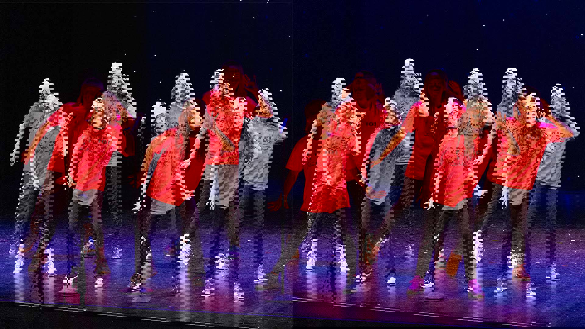 Young students in red shirts and puppy ear headwear performing on a dark stage. 