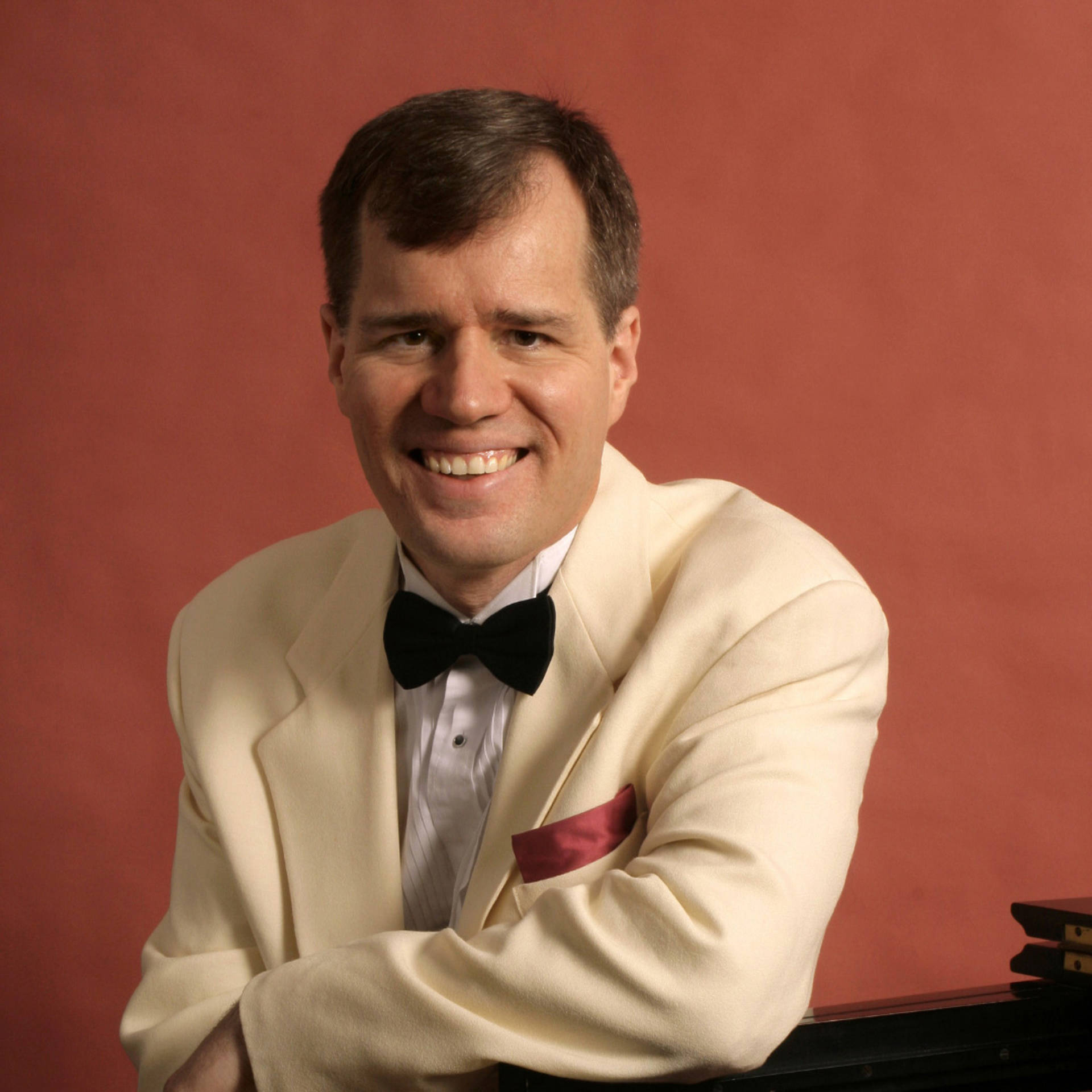 A white man with short brown hair and dark eyes in a white tuxedo with red handkerchief.