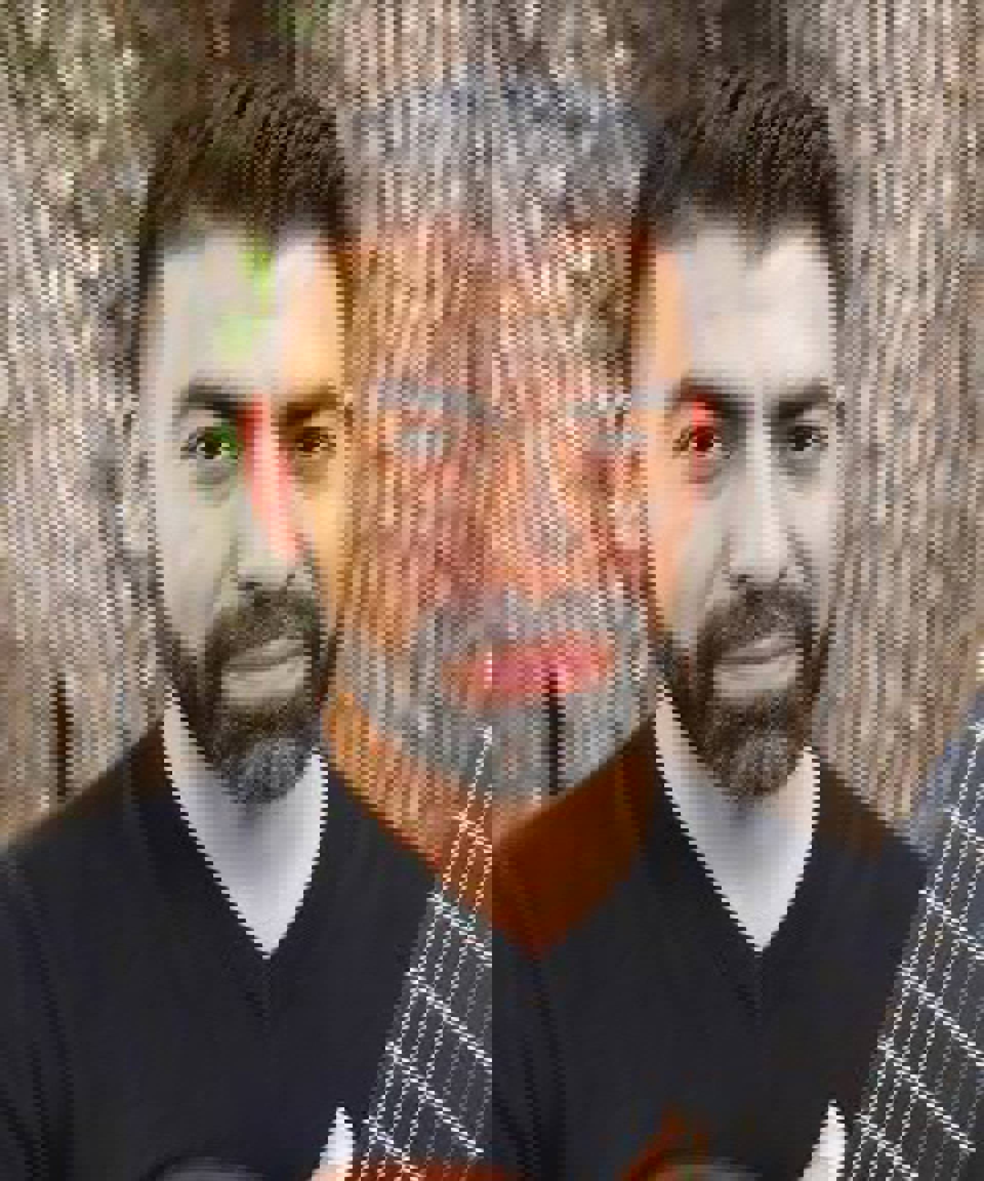 A middle aged man with dark hair and a beard. He is holding a guitar.