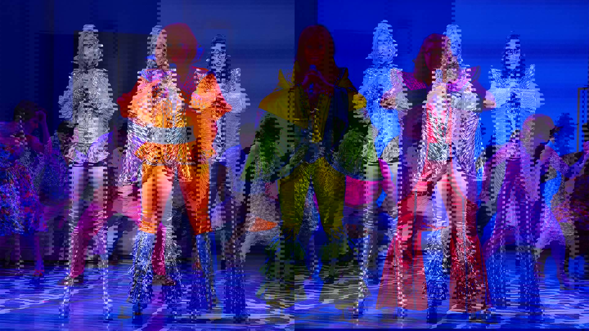 Three women in colorful shiny outfits singing into microphones.