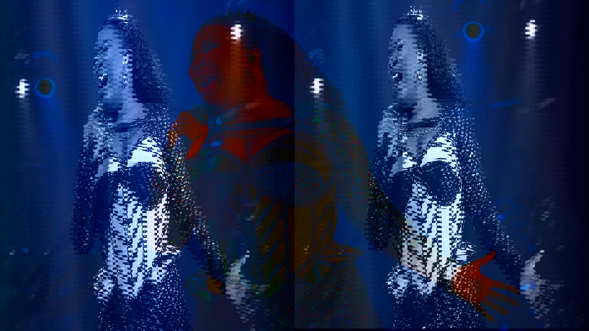 An African American woman in futuristic glittery outfits and holding a microphone, performing on stage