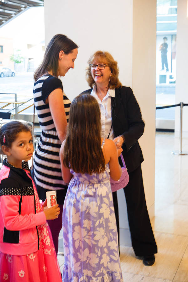 A woman and two young girls talk to an overture usher. The usher is a middle aged woman in a dark outfit with a white shirt.