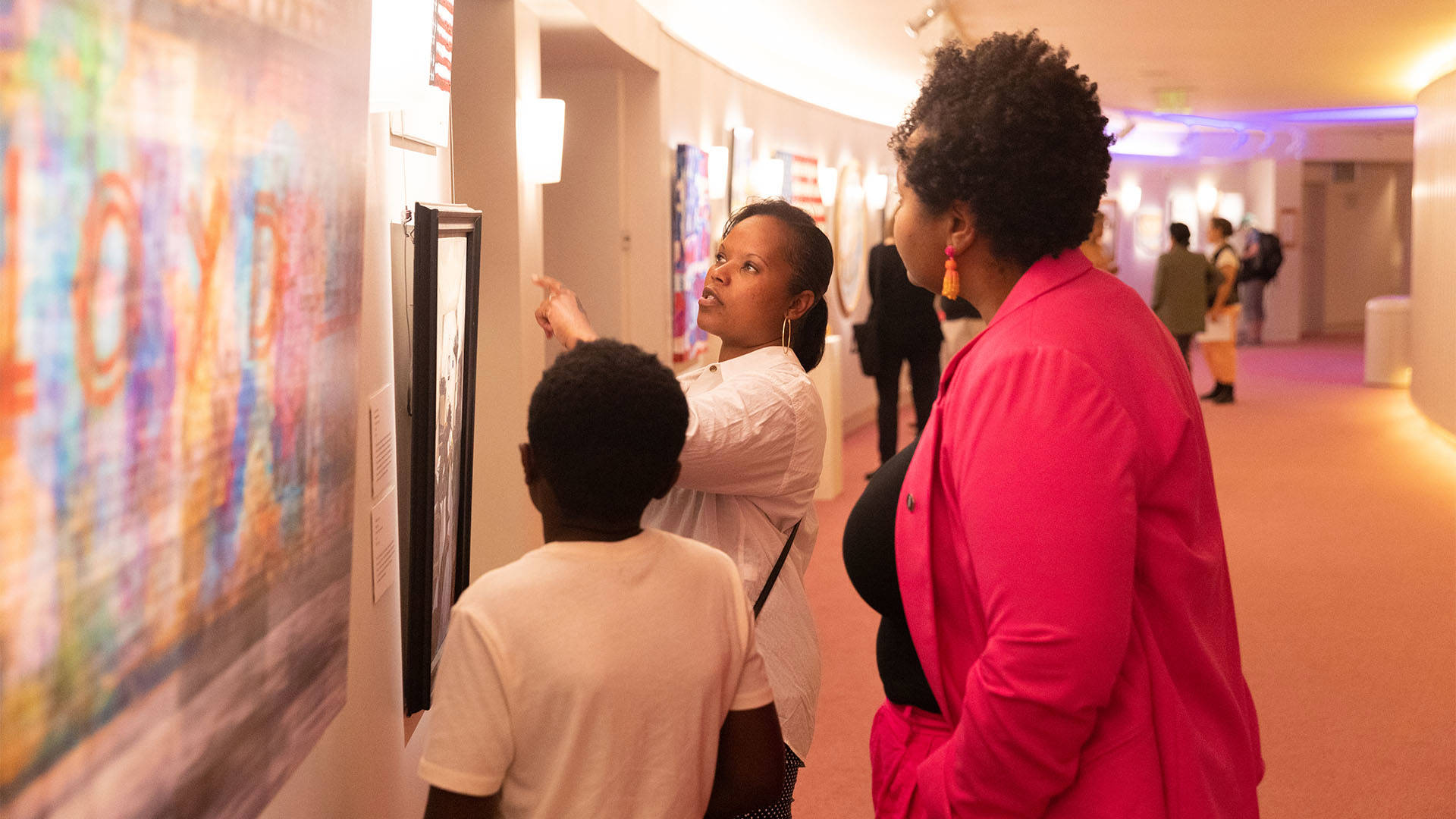 Three people look at art on a gallery wall.
