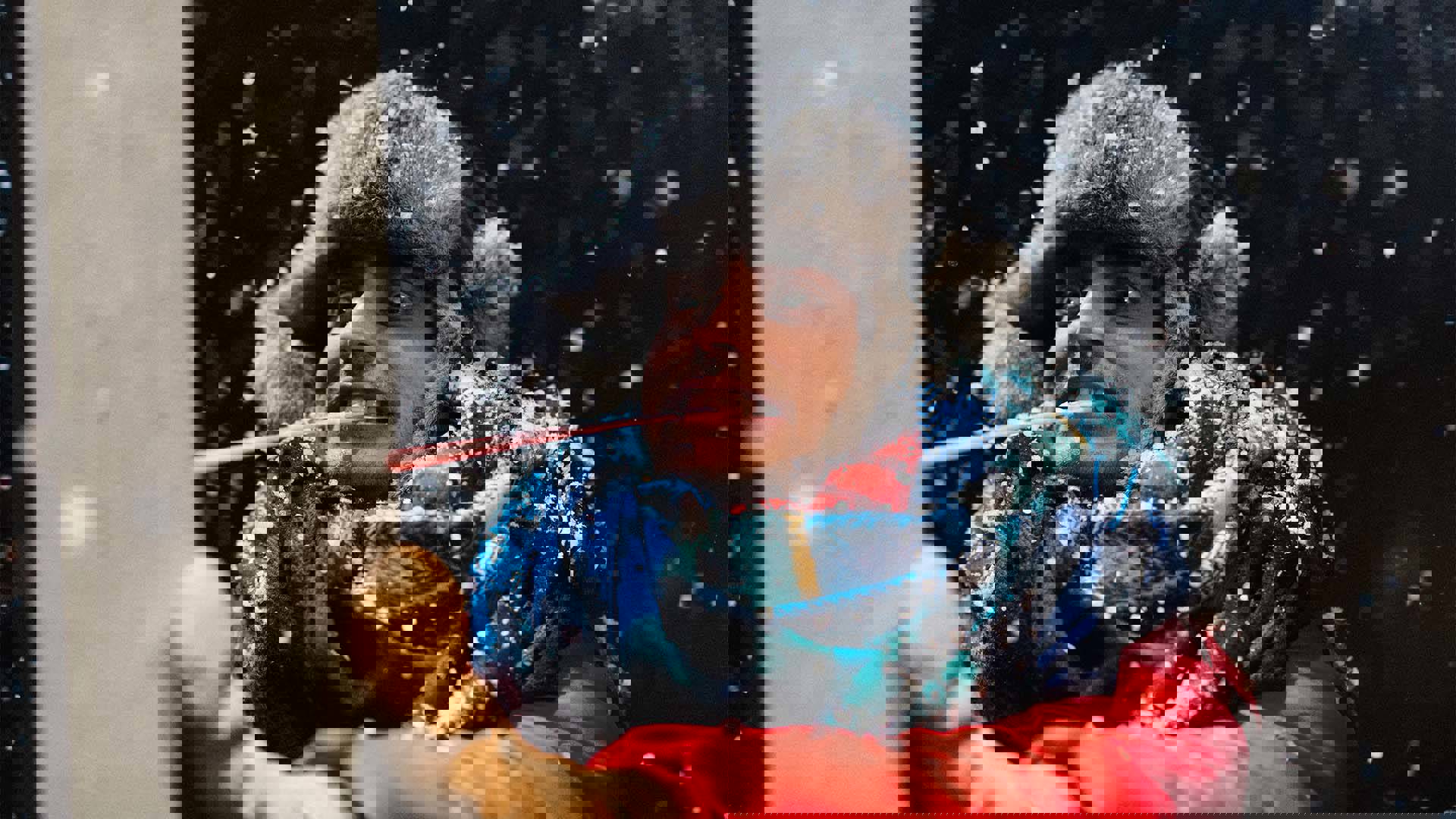 A performer wearing a winter hat, scarf and red puffy coat sticking a ridiculously long tongue onto an icy pole.