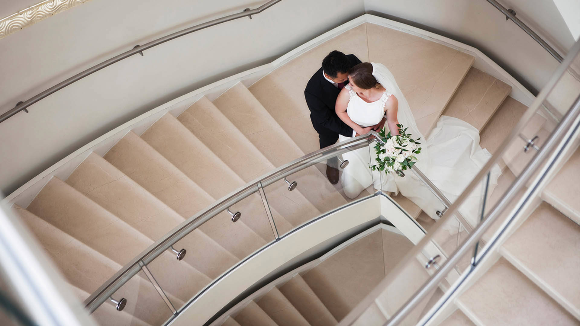 A bride and groom standing on a staircase. The photo is taken from above.