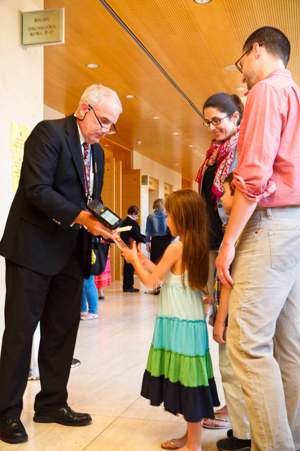 A man woman and child get their tickets scanned by a middle aged man in a dark suit and glasses.
