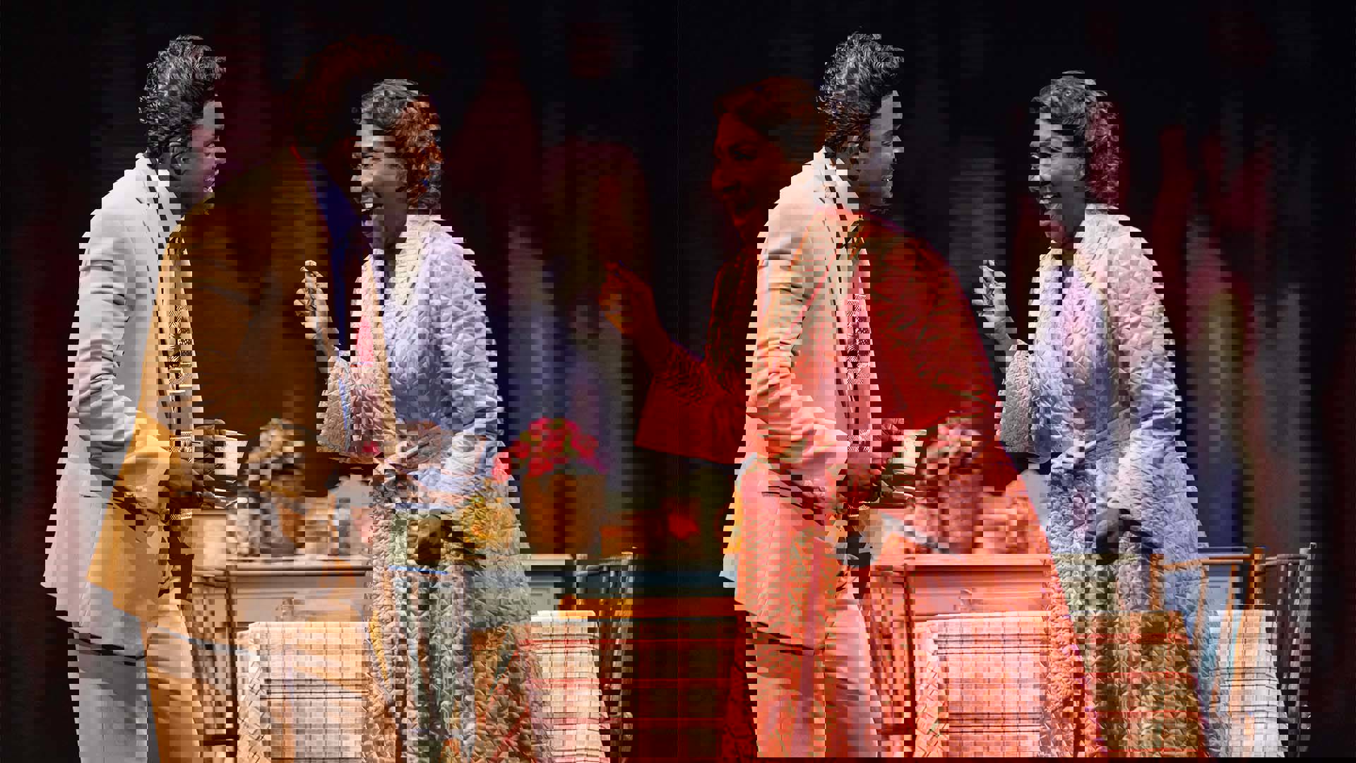 An African American man in a tan suit holding an African American woman's hands in his. She is wearing a pink robe.