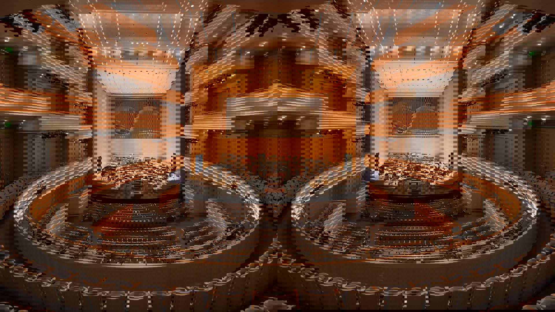 Overture Hall empty. A view from the second level looking on a stage filled with chairs and music stands. Behind the stage are organ pipes.