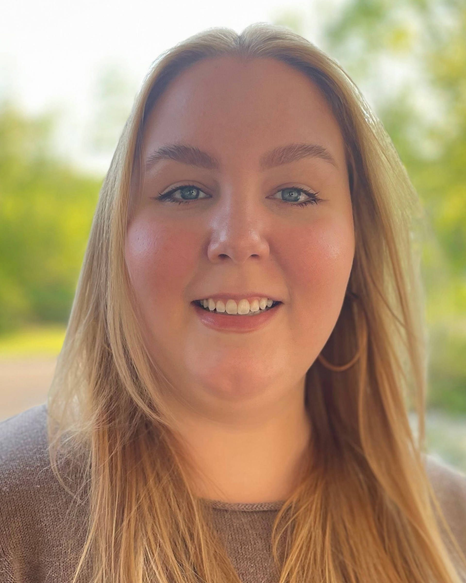 Headshot of a caucasian woman with long blonde hair and blue eyes. She is smiling and wearing a grey shirt.
