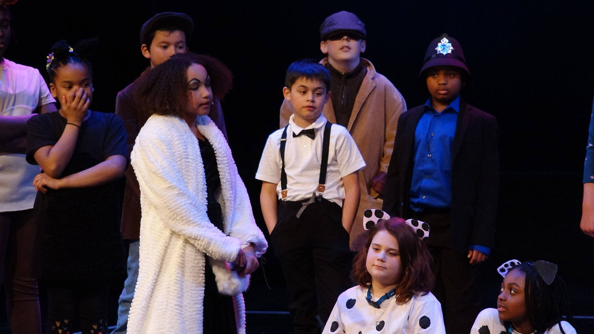 A group of children in various costumes performing on stage