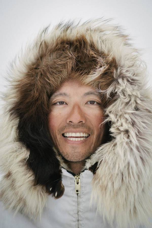 Photographer Kiliii Yuyan smiles into the camera. He is wearing a white coat with a fur hood.