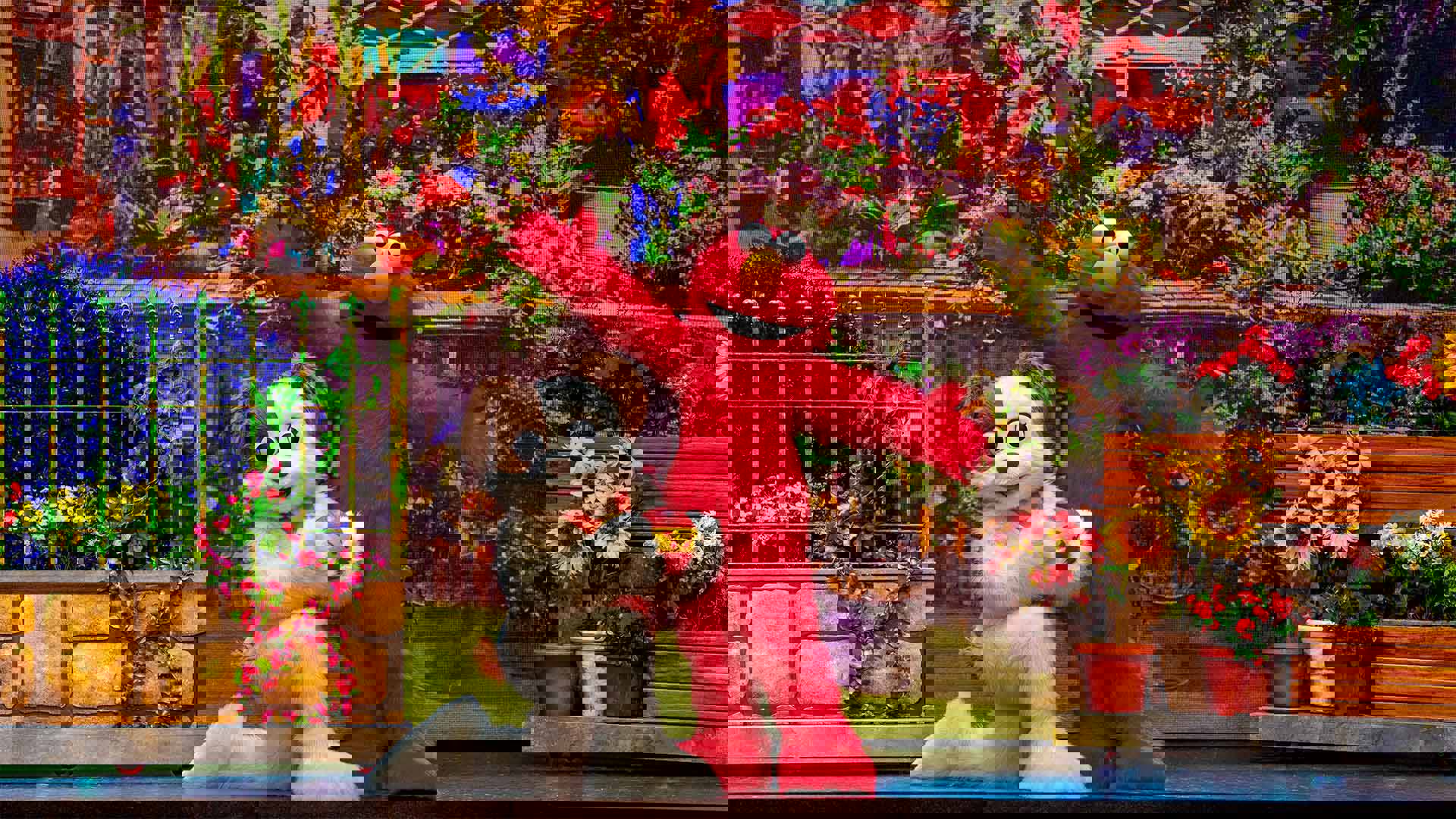 a performer in an Elmo costume, a red furry Jim Henson character with an orange nose, with a kneeling performer in a dog outfit against a background with flowers.