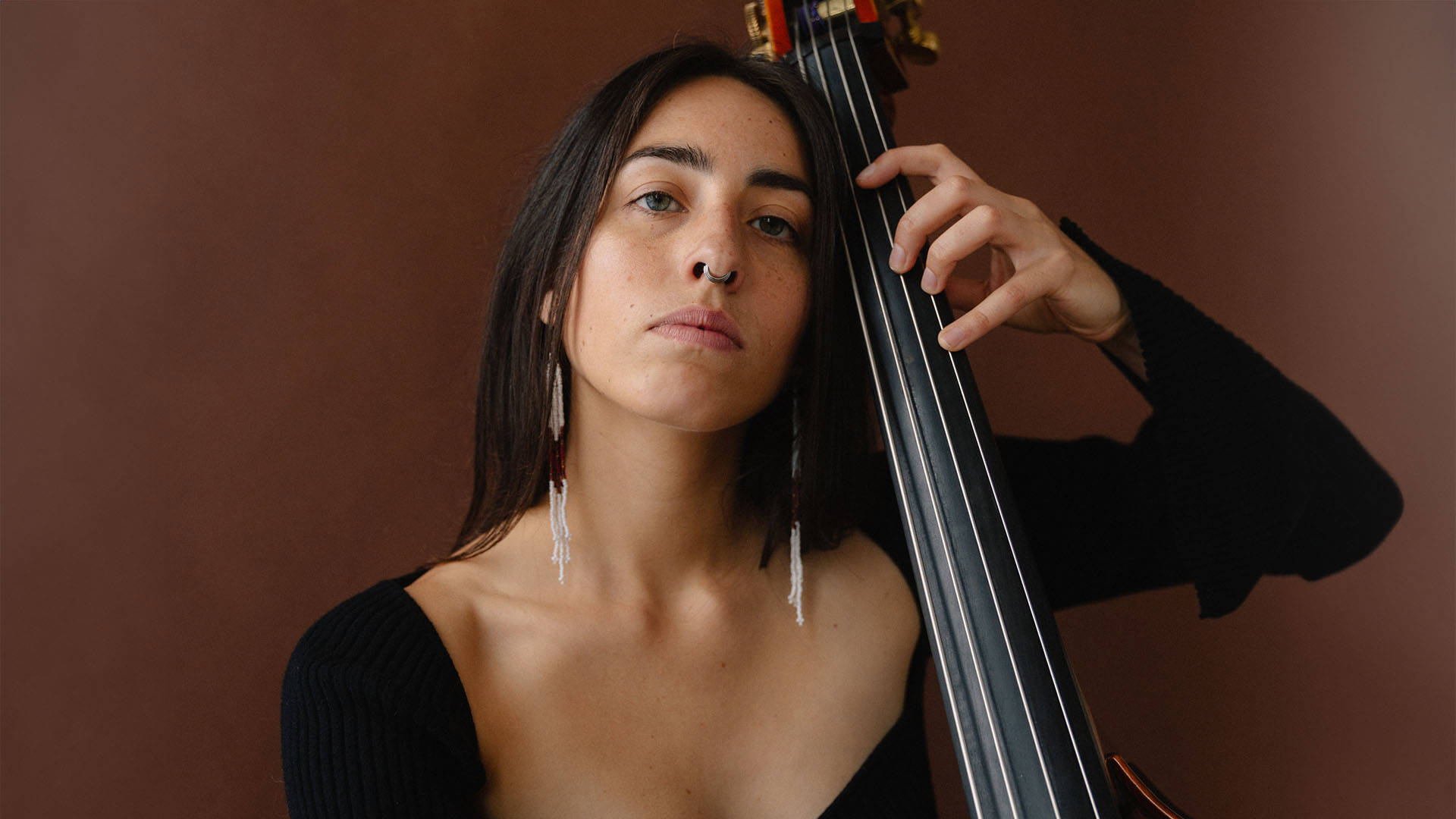 Headshot of a woman with long dark hair, blue eyes and medium complexion playing the neck of a double bass.