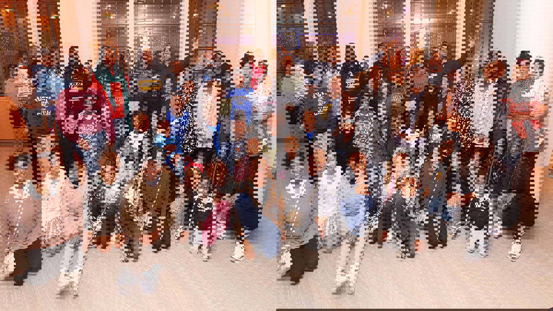 A group of smiling adults and children posing together in front of large windows and white columns