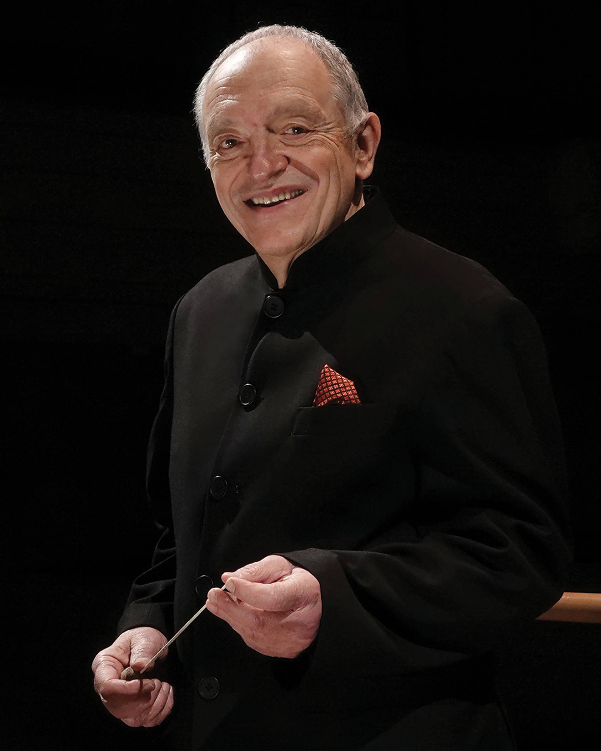 Headshot of an older caucasian man with short grey hair, dark eyes and a modern black suit.