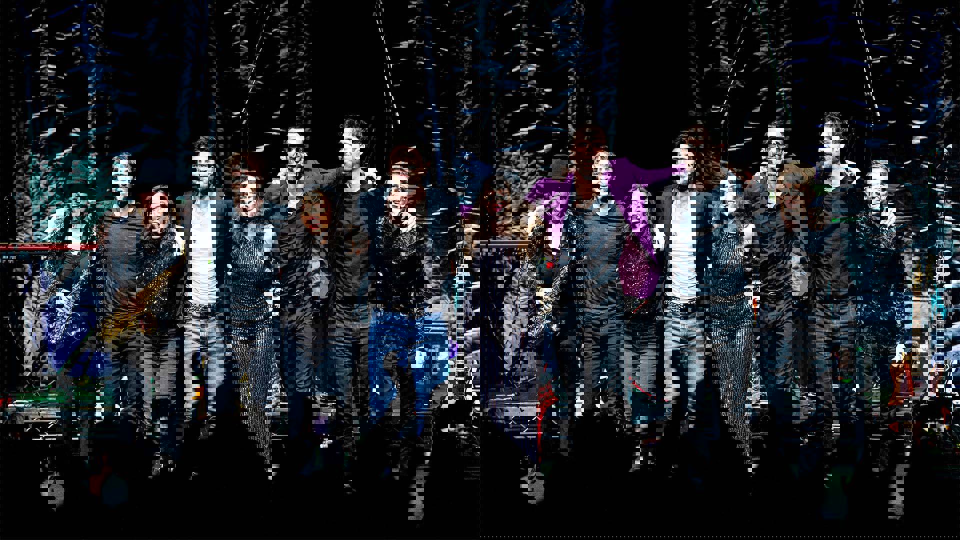 A band on stage standing together for a cheering crowd.