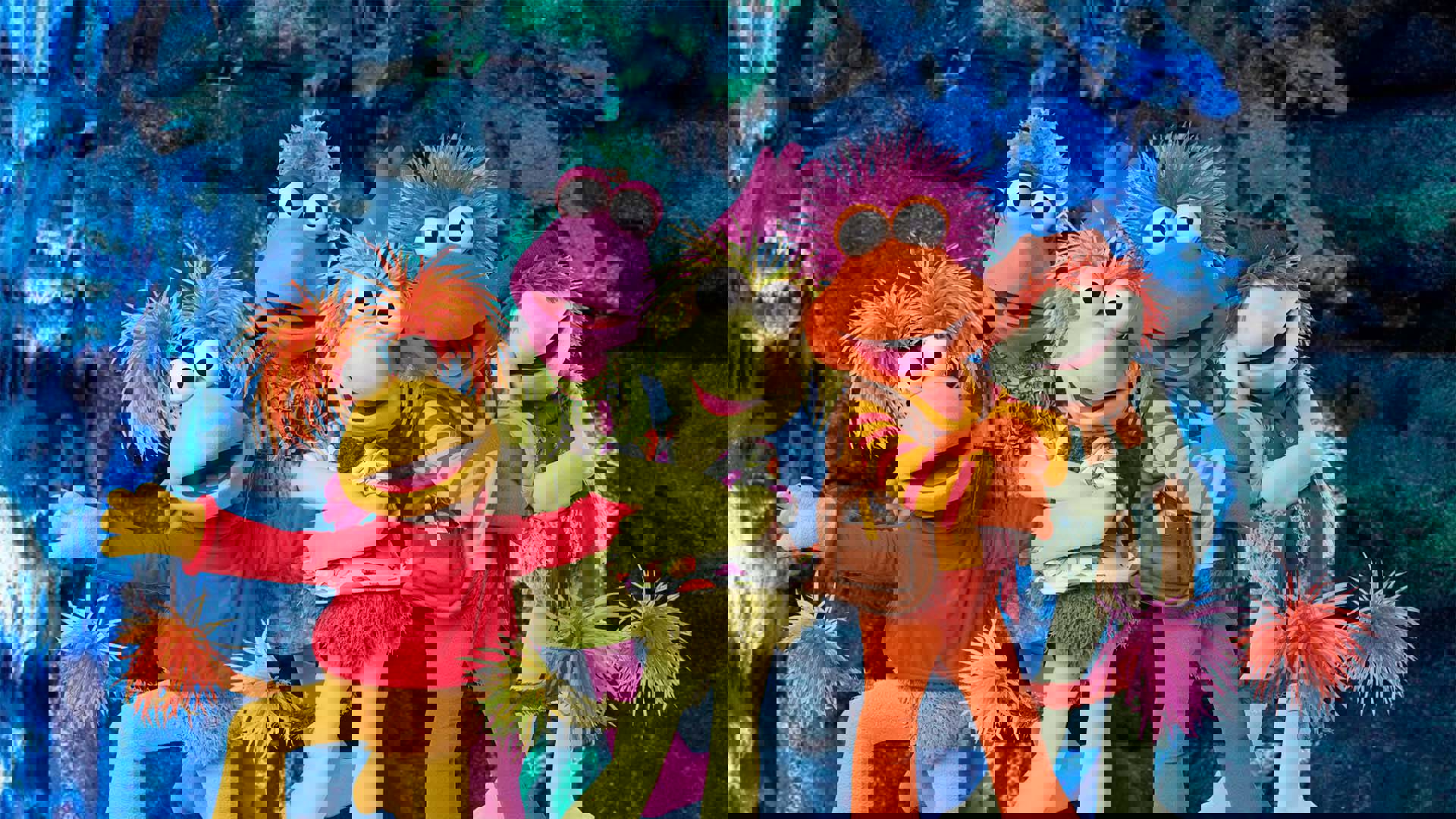 Five puppets with colorful poofy messy hair and large white eyes with black pupils are posing together against a blue-lit cave wall.