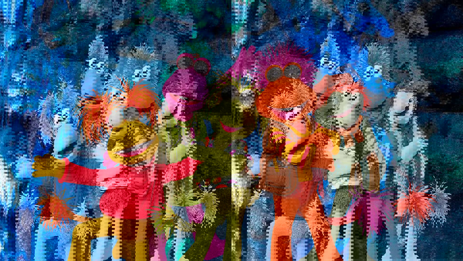 Five puppets with colorful poofy messy hair and large white eyes with black pupils are posing together against a blue-lit cave wall.