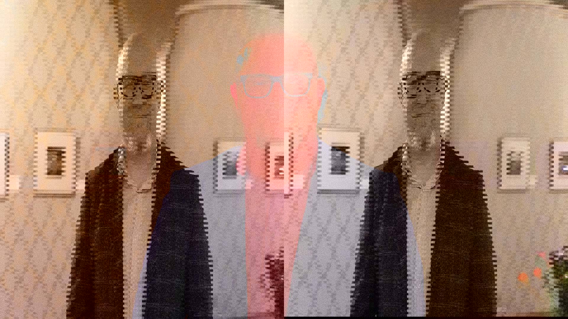 Headshot of a smiling middle aged man with light complexion, a bald head and a white and red beard.