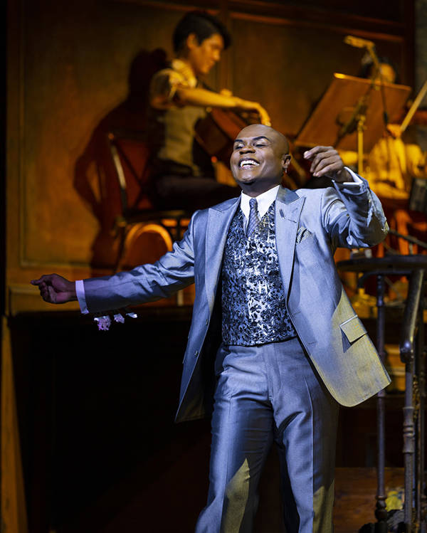 A bald African American man in a silver suit dances.