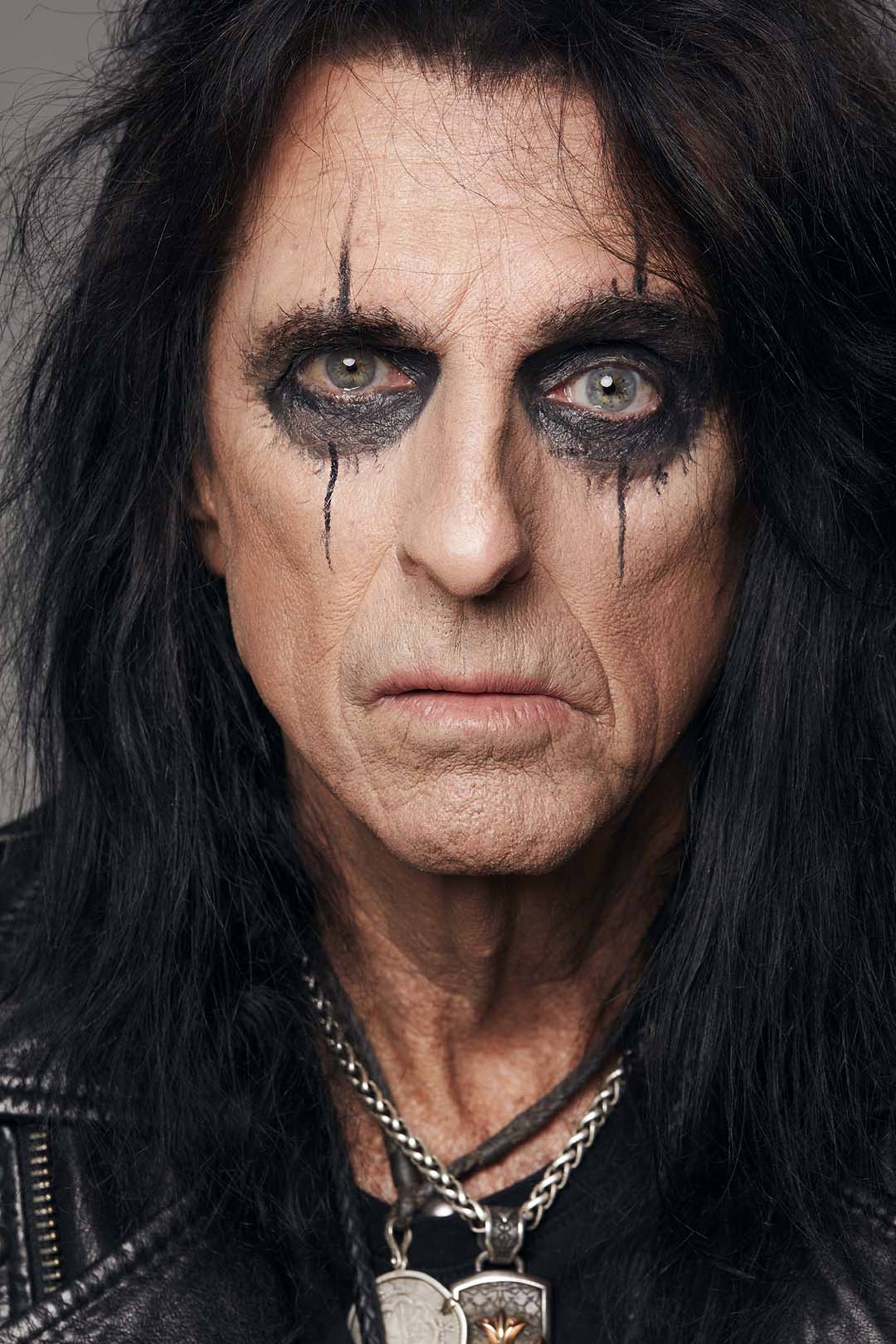 A close up of an older man with long black hair and a lot of eye shadow. 