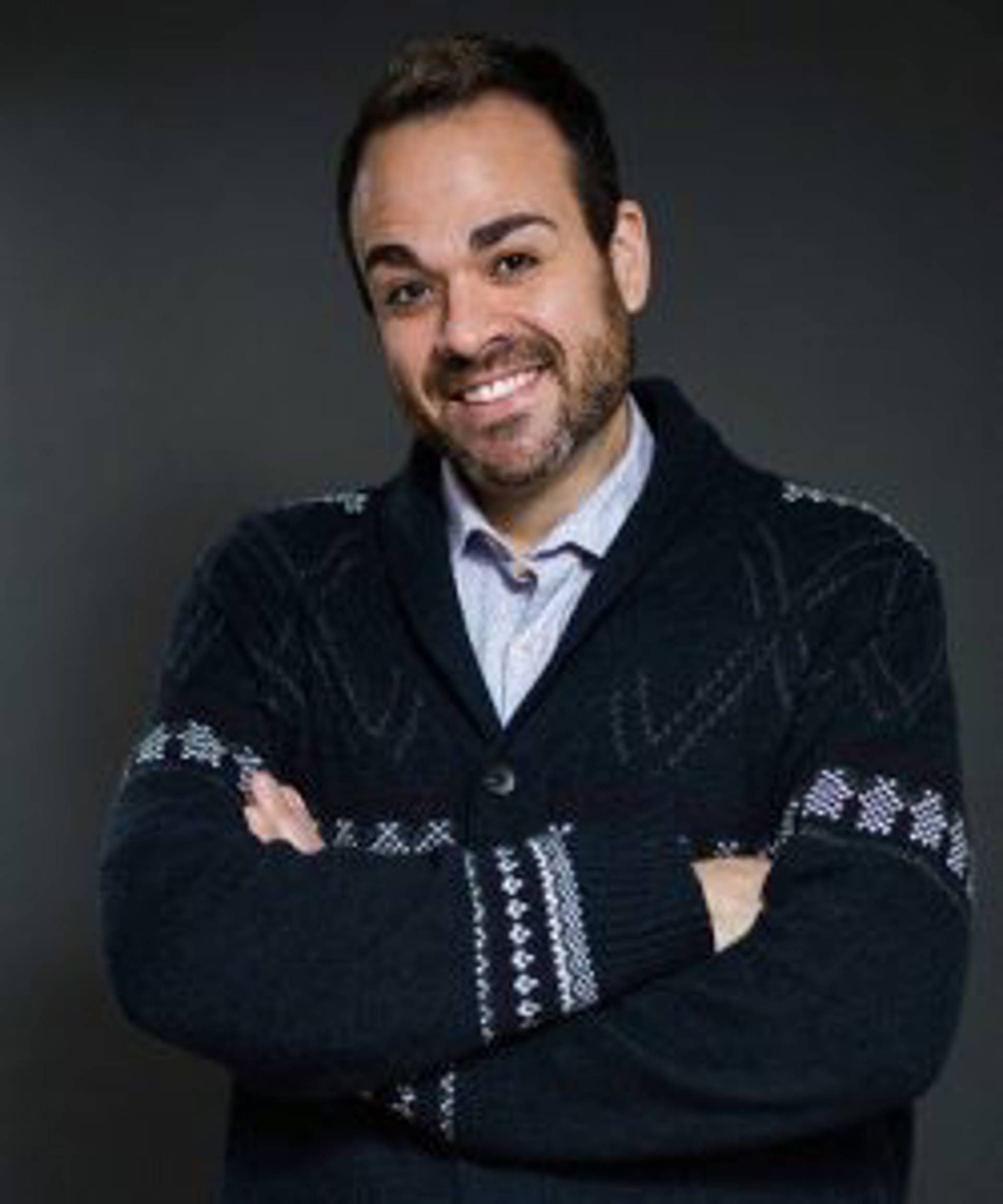 Headshot of a caucasian man with short dark hair and a sweater on, folding his arms.