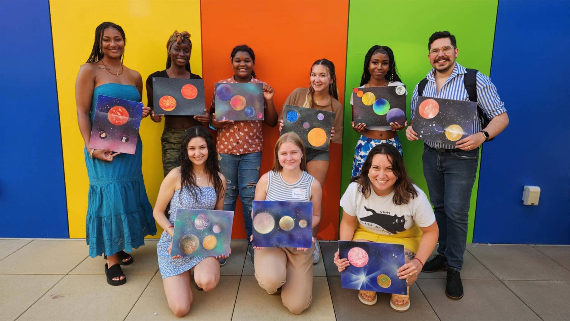 students posing for a photo, holding colorful pieces of painted art.