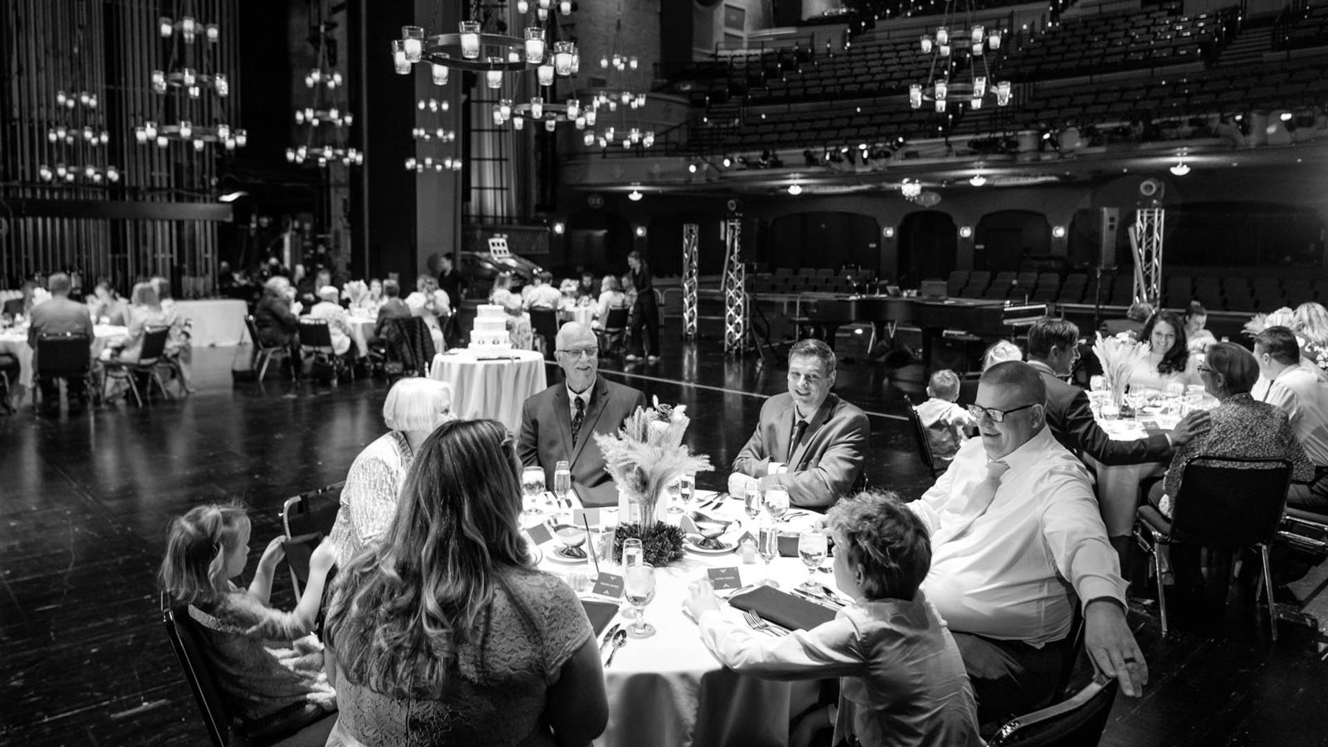 Grayscale photo of several dozen people seated at circular tables on Capitol Theater stage.