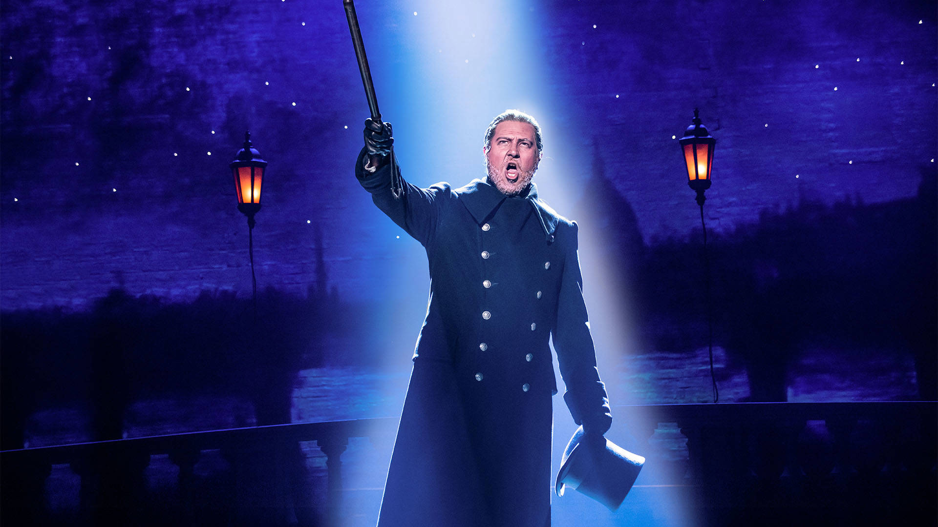 A man in an imposing officers coat holding a tophat and a cane. Singing.