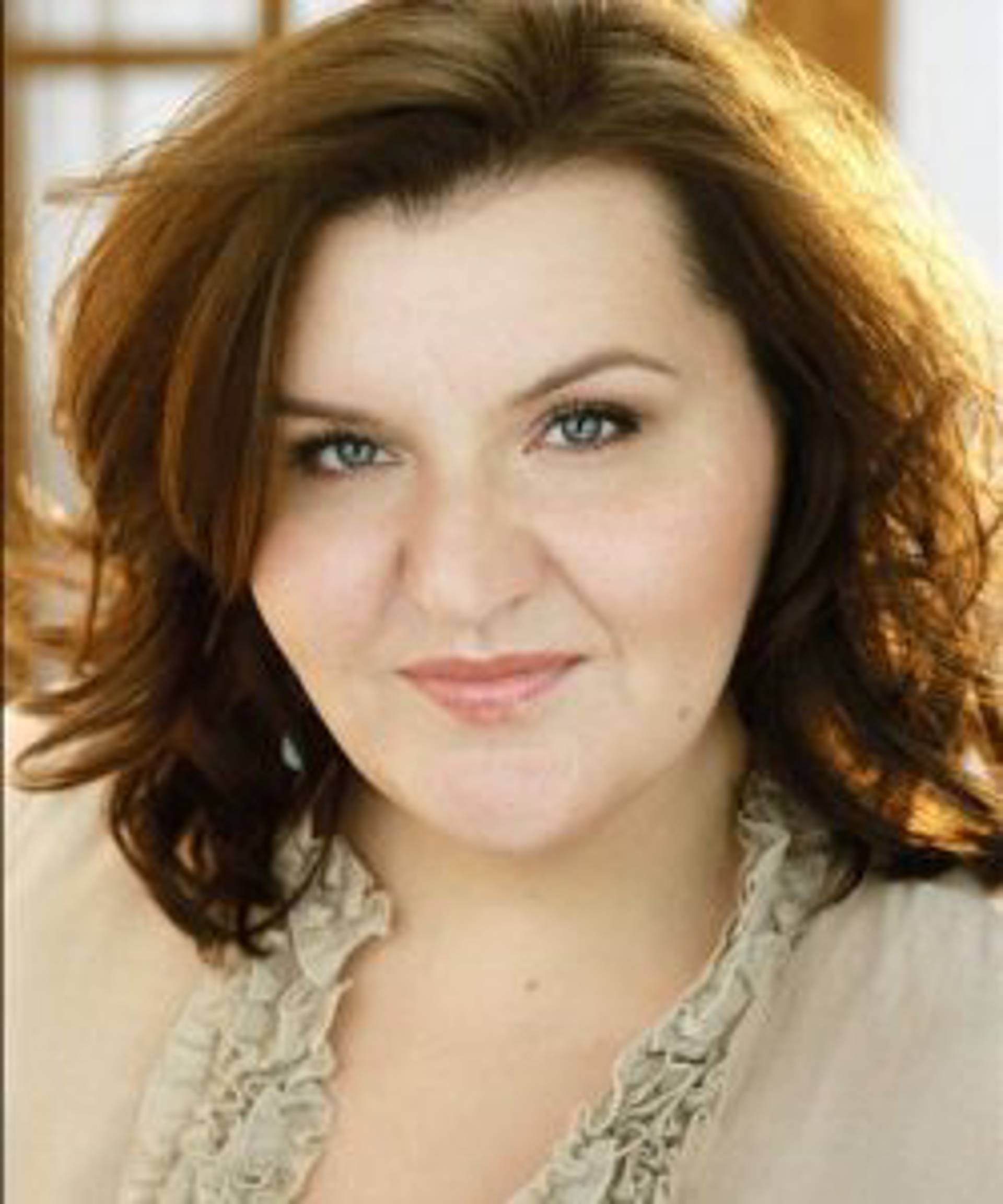 Headshot of a caucasian woman with red hair and grey eyes in a light top.