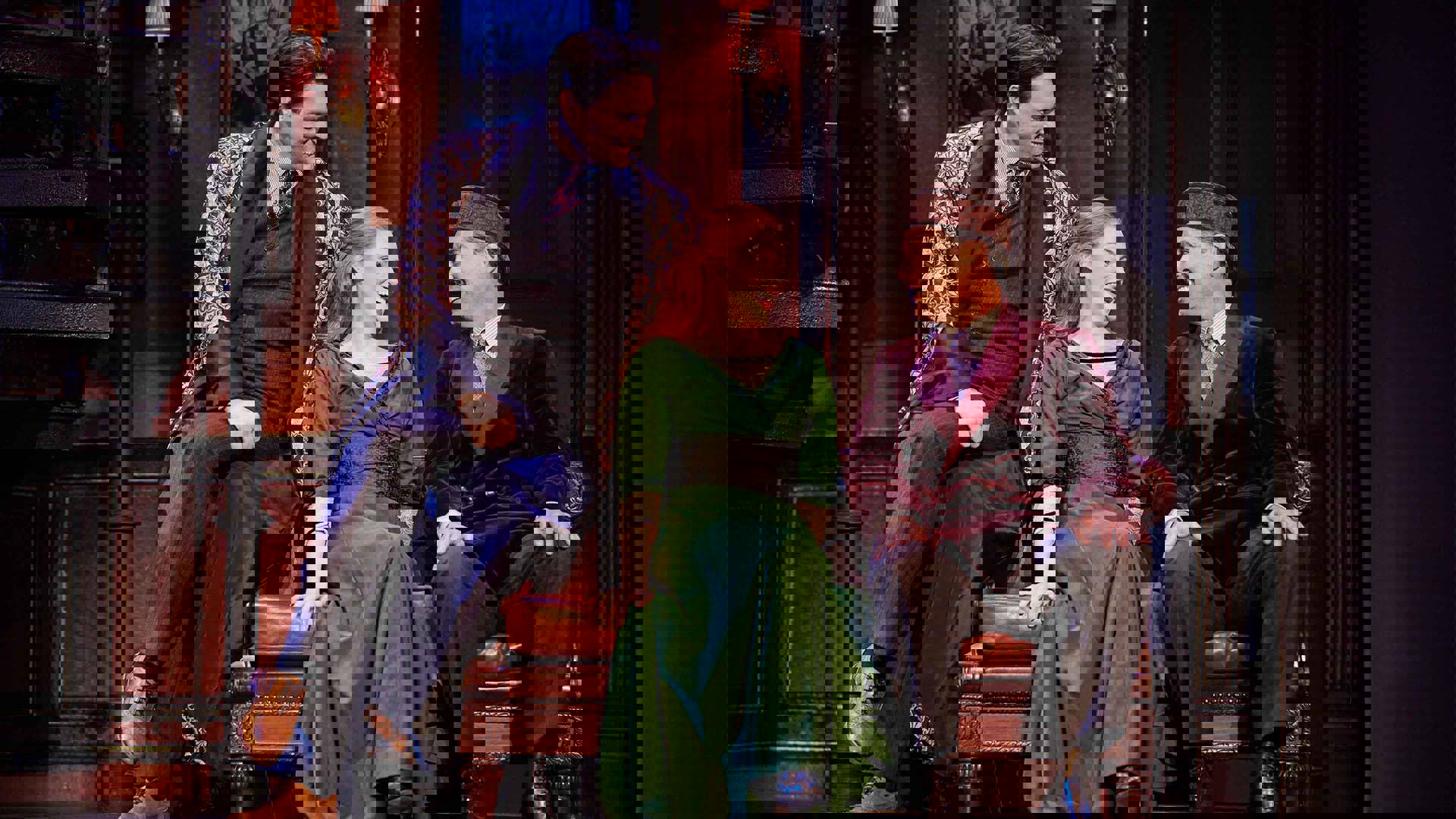 Two men and a woman with red hear and a green dress sit on a leather sofa smiling at each other