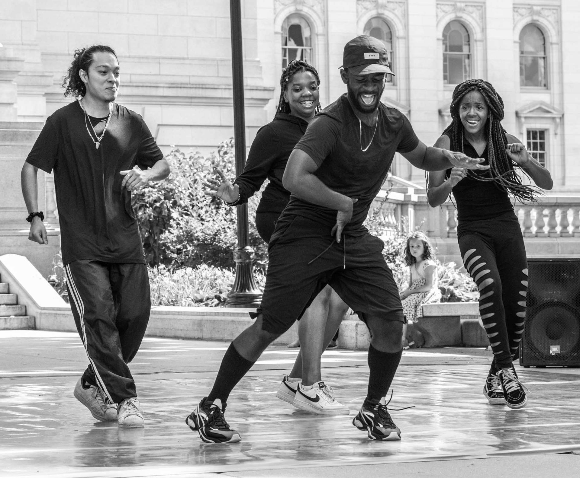 A black and white photo dancers outside of the Madison capitol building. They are dressed in black street clothes.