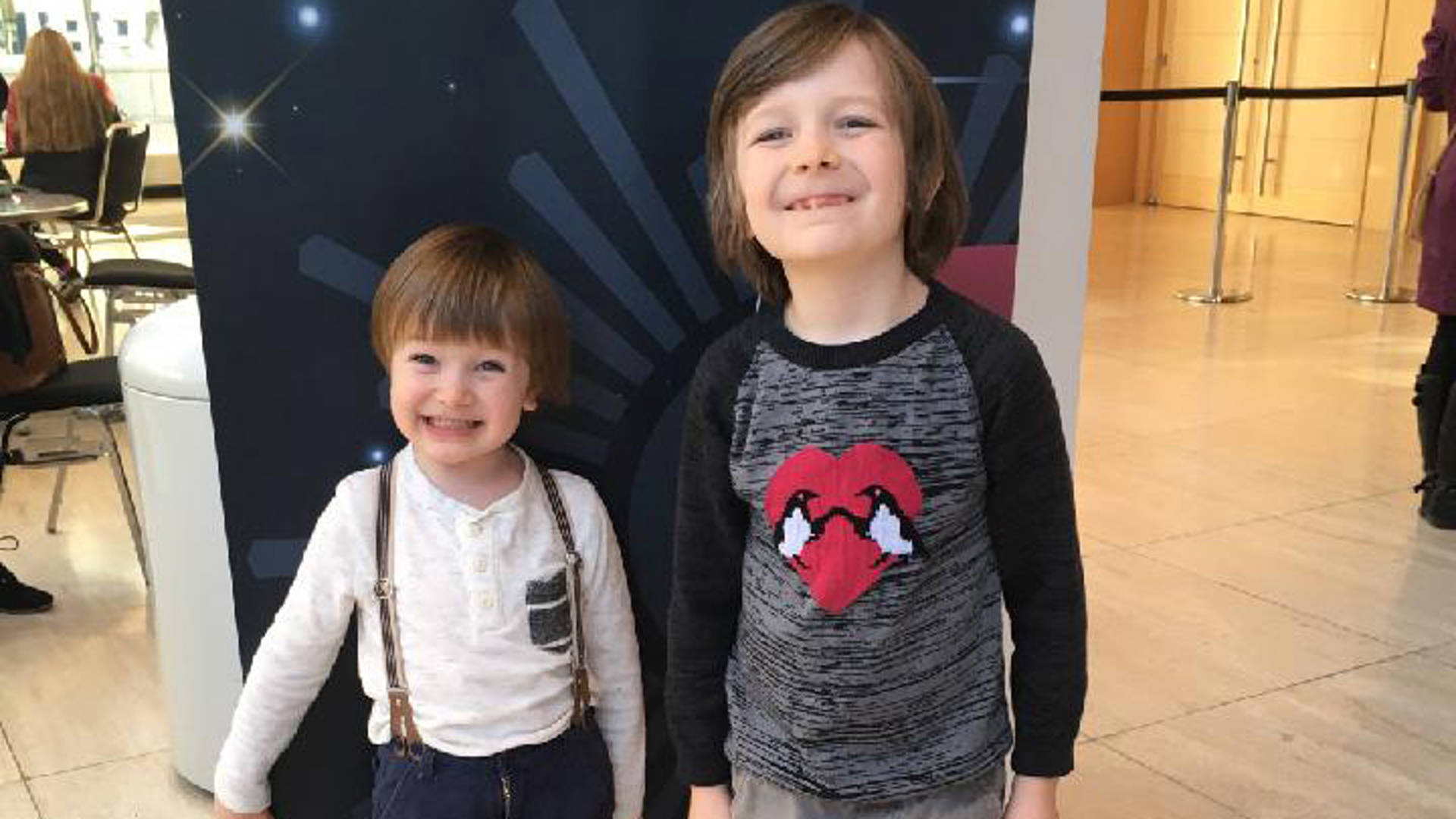 Two young kids smile for a portrait in Overture Hall Lobby. They both have dark eyes and brown hair.