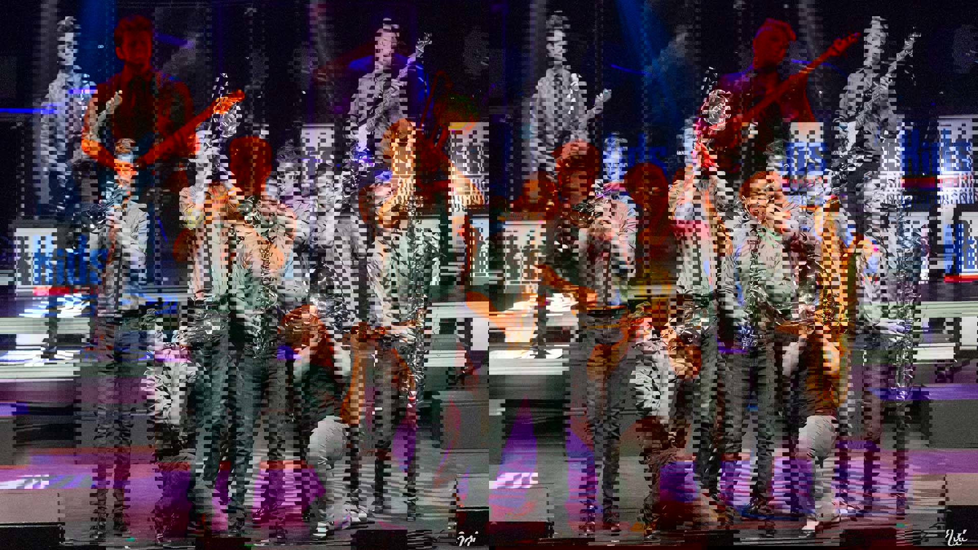 A group of high schoolers in matching grey shirts and ties holding various instruments and stiking poses as they play.