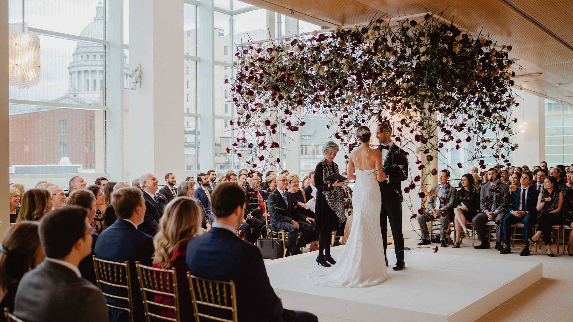 A wedding ceremony in a large hall. The Wisconsin Capitol building is in the background.