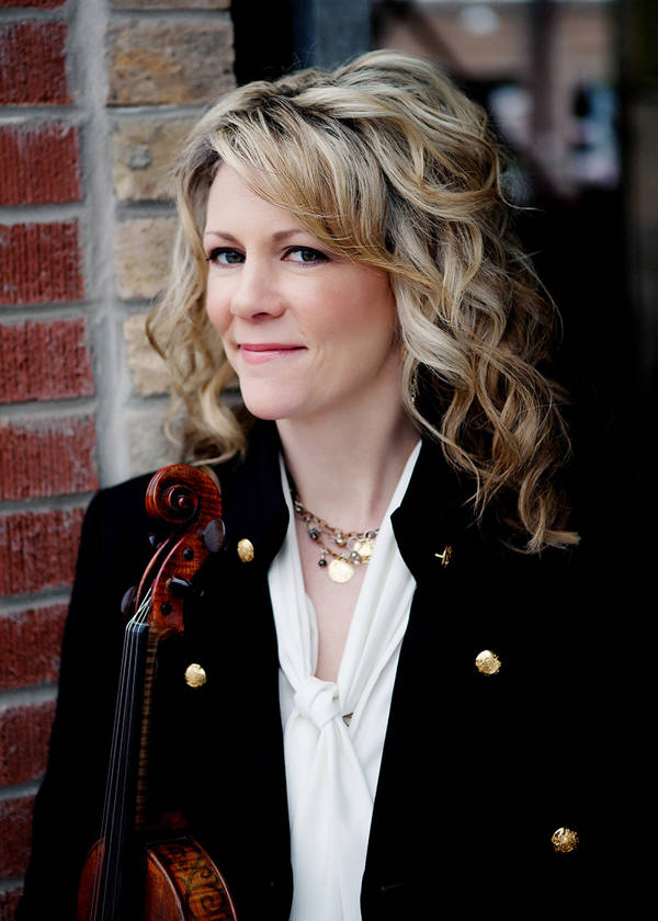 Headshot of a caucasian woman with blonde hair and brown eyes. she is wearing a dark jacket with gold buttons over a white blouse and is resting a violin against her torso.