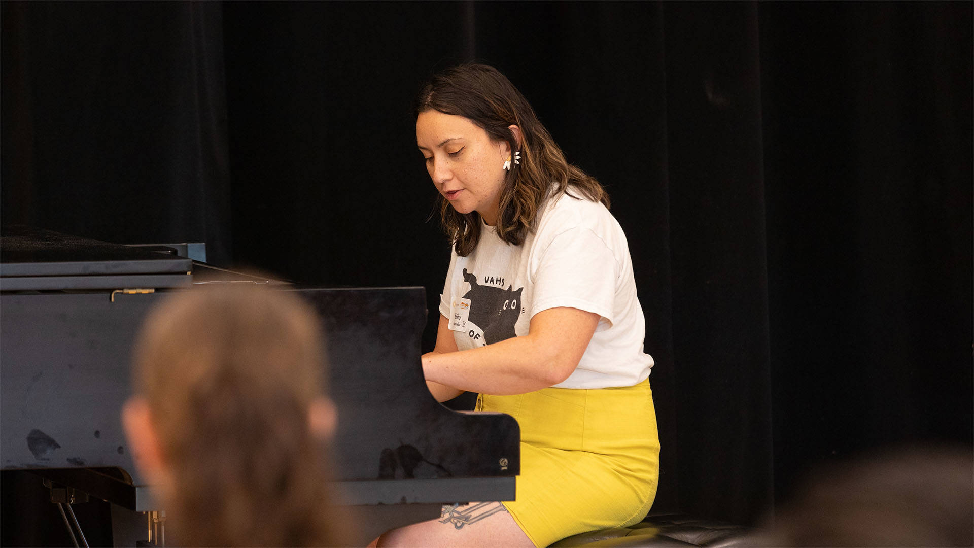 A woman with medium complexion and long brown hair playing piano.
