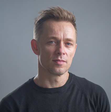 Headshot of a young caucasian mand with short blond hair and a black tshirt.