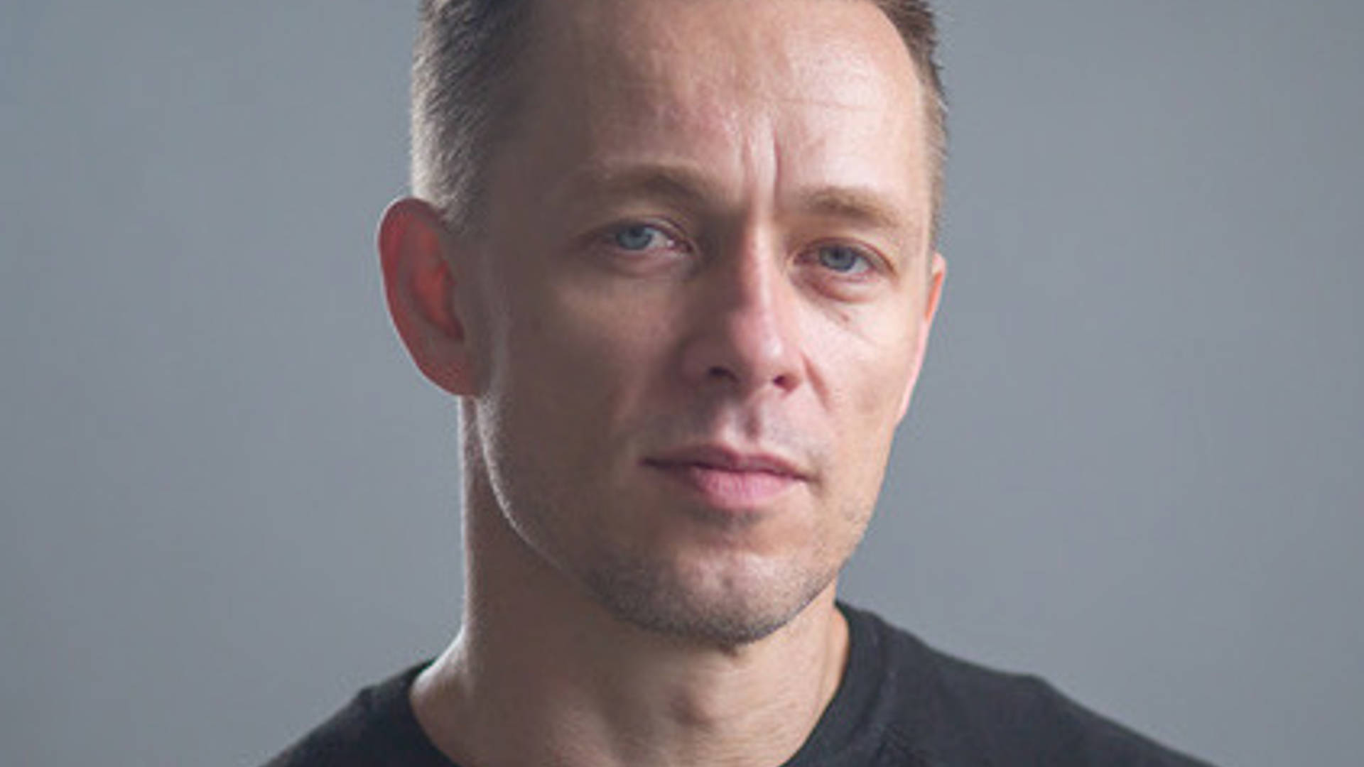 Headshot of a young caucasian mand with short blond hair and a black tshirt.
