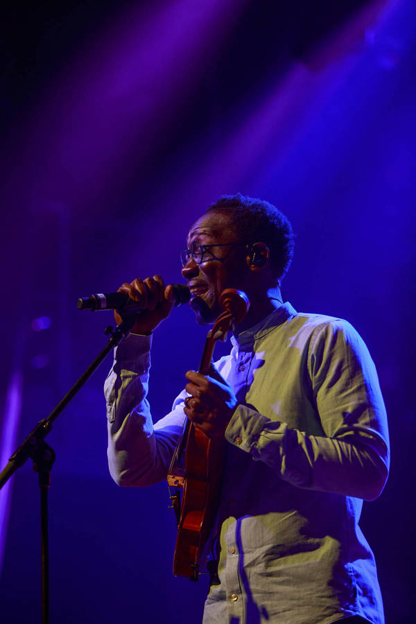 Photo of Will Baptiste performing on stage. He is singing into a mic while holding a violin.
